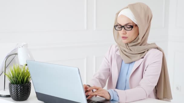 Втомлена мусульманка в окулярах в кінці робочого дня друкує на ноутбуці . — стокове відео