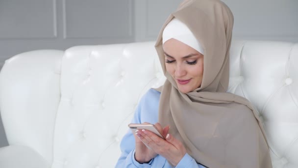 Muslimische Frau im Hidschab plaudert im Smartphone und lacht. — Stockvideo