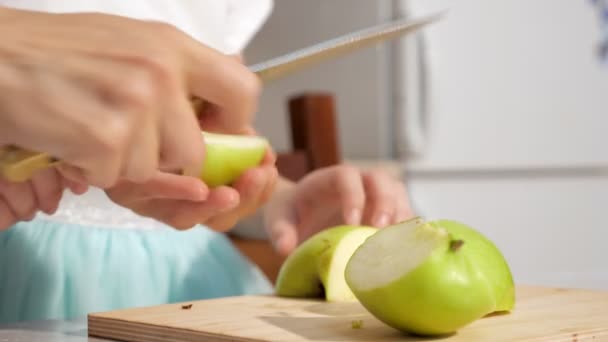 Mamá enseña y le muestra a su hija cómo cortar manzana en trozos pequeños . — Vídeos de Stock