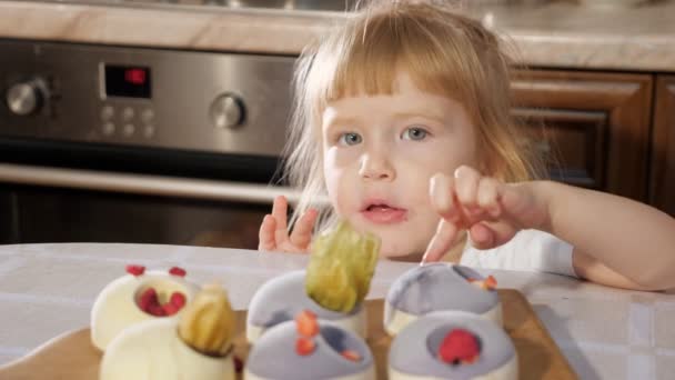 Pequeña linda chica está decorando pequeño pastel con frambuesa . — Vídeos de Stock