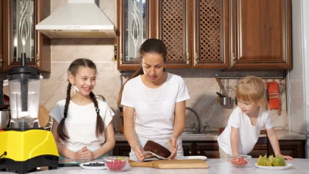Mamá está horneando un pastel con sus dos hijas en la cocina . — Vídeos de Stock