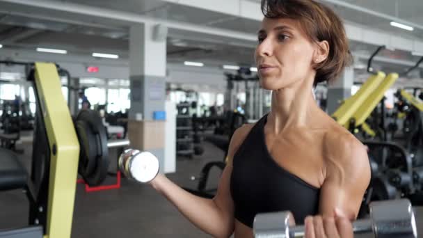 Спортивна зріла жінка робить біцепси вправи з гантелями в спортзалі . — стокове відео