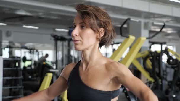 Deportiva en ropa deportiva extiende sus manos a un lado con mancuernas en el gimnasio . — Vídeos de Stock