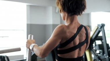 Kadın kürek makinesinde omurga kasları için egzersizler yapıyor, geri görünümü.