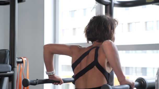 Mujer joven está haciendo flexiones en bares irregulares en el gimnasio . — Vídeos de Stock