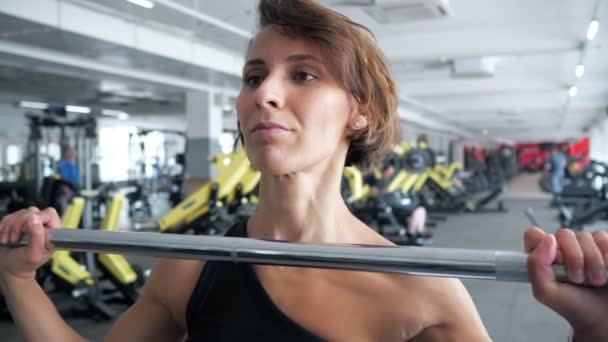 Donna sta facendo insieme di ripetizioni esercizio con bilanciere sollevandolo sopra la testa in palestra . — Video Stock