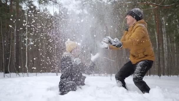 Par, flicka och kille, kastar en snö varandra i vinterskogen i slow motion. — Stockvideo