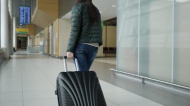 Gezgin kadın bavul taşıyan modern havaalanı terminalinde yürüyor, arka görünüm.