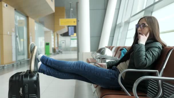 Znudzony młoda kobieta czeka jej lot na lotnisku siedzi w hali. — Wideo stockowe