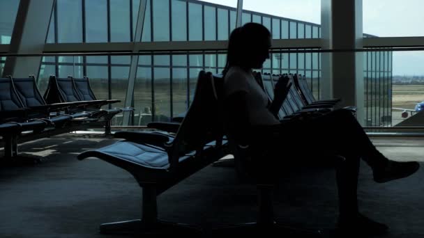Kobieta siedzi i przegląda smartfon w pustej poczekalni na lotnisku. — Wideo stockowe