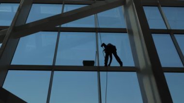 Adam yüksek katlı bir binanın pencerelerini temizliyor..