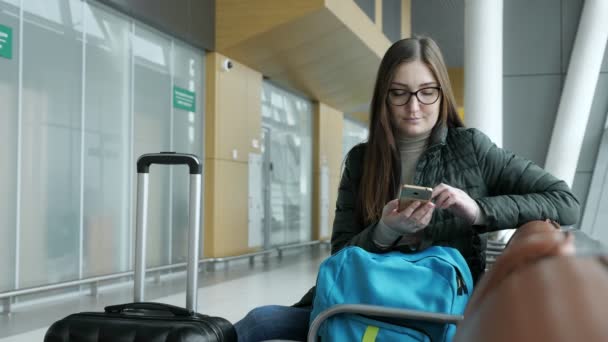 Молодая женщина проходит электронную регистрацию в смартфоне, ожидая свой рейс в аэропорту . — стоковое видео
