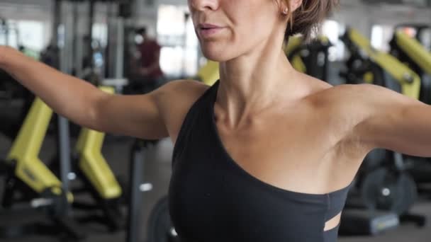 Sportieve vrouw in sportkleding spreidt haar handen aan de zijkant met dumbbells in de sportschool. — Stockvideo