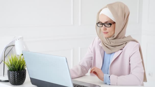 Vermoeide moslim vrouw werkt en types op laptop, zet haar bril uit en wrijft haar ogen. — Stockvideo