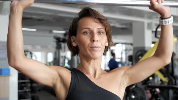 Donna sta facendo insieme di ripetizioni esercizio con bilanciere sollevandolo sopra la testa in palestra . — Video Stock