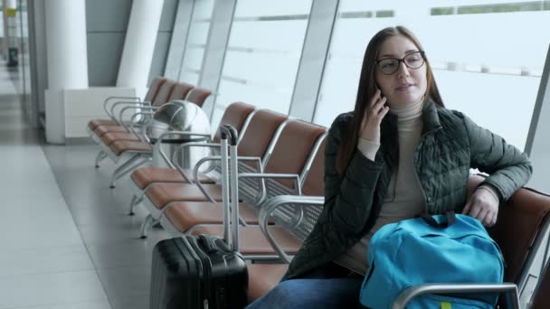Happy woman is talking on mobile phone waiting her flight in airport. — Stock Video
