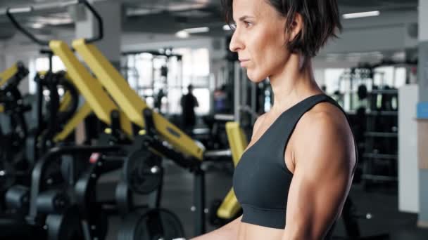 Deportiva mujer madura está haciendo ejercicio bíceps con mancuernas en el gimnasio . — Vídeo de stock