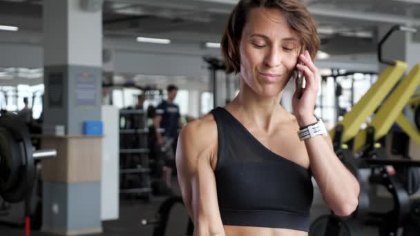 Mogen kvinna gör biceps övning med hantlar i gym och talar telefon. — Stockvideo