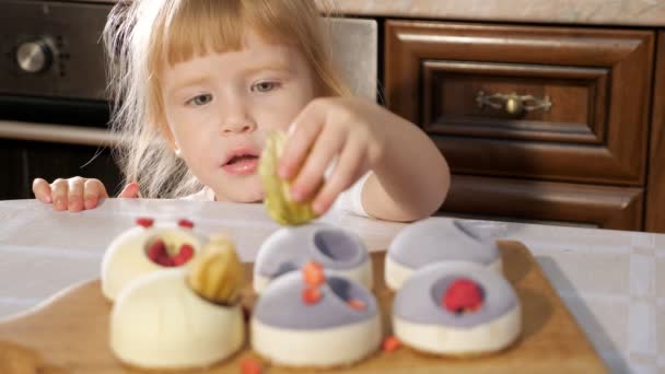 Pequeña linda chica está decorando pequeño pastel con frambuesa . — Vídeos de Stock