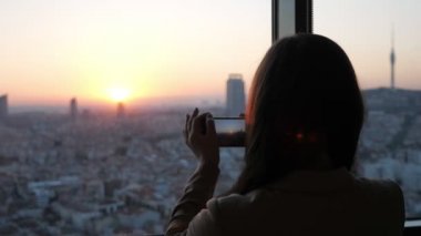 Kadın gökdelen onu modern düz akıllı telefonda gün batımında panoramik şehir görünümü fotoğrafları çeker.