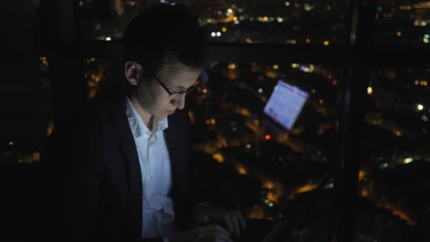 Молодой человек фрилансер работает за компьютером возле окна в доме ночью . — стоковое видео