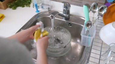 Kadın evde mutfakta elleriyle çatal bıçak yıkıyor.