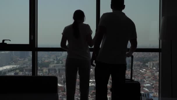 Silhuett av glada unga par in i hotellrum med panoramautsikt över staden. — Stockvideo