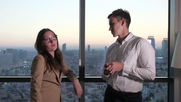 Collega's man en vrouw browsen smartphones staande in de buurt van panoramische raam in Office. — Stockvideo