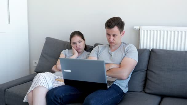 Bored sleepy couple man and woman are watching video on laptop sitting on sofa. — Stock Video