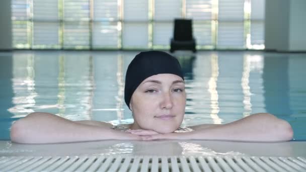 Jonge vrouw in Cap kijken naar camera en glimlachend in het zwembad. — Stockvideo