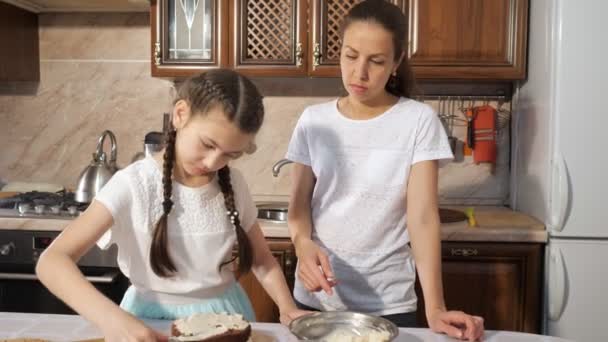 Madre con su hija adolescente está cocinando pastel de chocolate hecho a mano con crema juntos — Vídeos de Stock