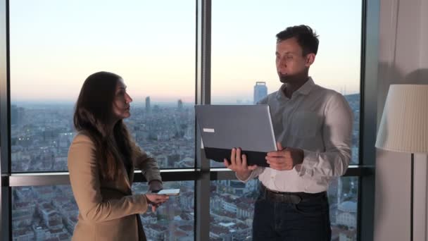 İş arkadaşları ofiste panoramik pencerede duran çalışma anlarını tartışıyor. — Stok video