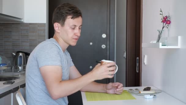 若い男性の旅行者は、賃貸アパートで小さなキッチンで朝食を食べている. — ストック動画