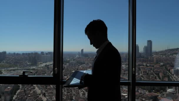 Silhouette üzletember dolgozik az ő laptop közelében panorámaablak városra néző. — Stock videók