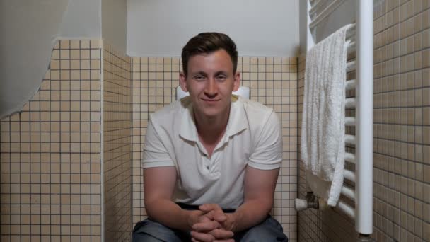 Молодий чоловік сидить на туалеті — стокове відео