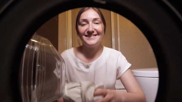 Счастливая домохозяйка загружает одежду в стиральную машину, вид изнутри . — стоковое видео