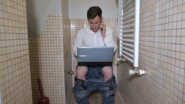 Jonge man workaholic werkt in toilet op computer praten op smartphone. — Stockvideo