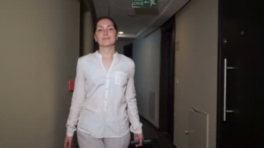 Mutlu kadın gezgin bavulile otel koridorunda yürüyor.