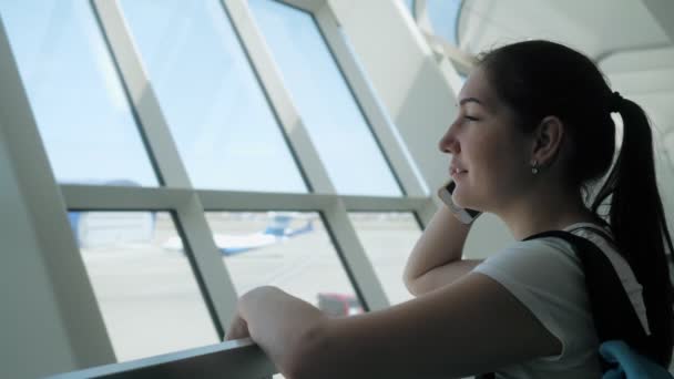 Mujer joven está hablando por teléfono móvil en la terminal del aeropuerto en la zona de vuelo . — Vídeos de Stock