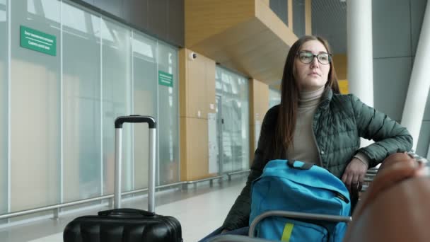 Young woman in glasses is waiting her flight in airport sitting in hall. — Stock Video