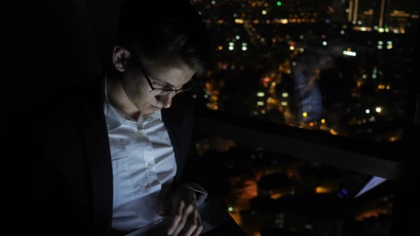 Fiatalember szabadúszóként dolgozik a számítógépén az ablak közelében otthon éjjel. — Stock videók