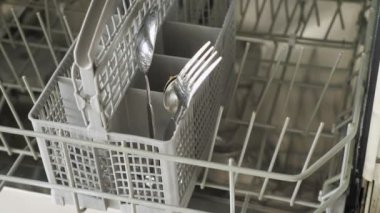 Adam bulaşık makinesine kirli tabaklar ve çatal bıçak takımı koyar.