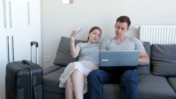 Man and woman choosing and booking tour and hotel sitting on sofa with passports and suitcase. — Stock Video