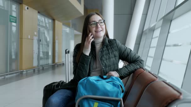 Щаслива жінка розмовляє по мобільному телефону, чекаючи свого польоту в аеропорту . — стокове відео