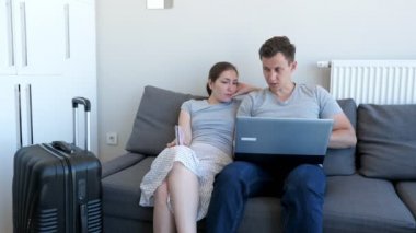 Pasaport ve bavul ile kanepede oturan erkek ve kadın seçimi ve rezervasyon tur ve otel.