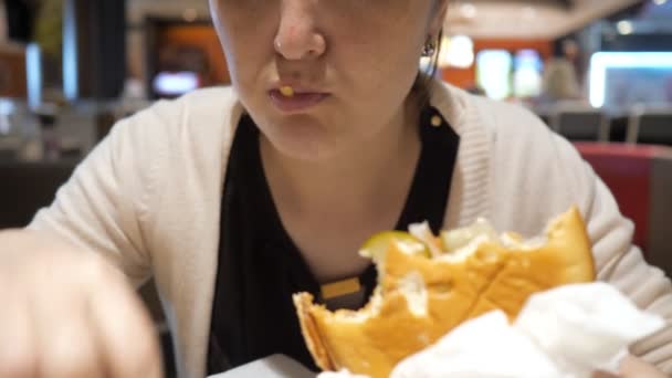 Žena, která žere hranolky a hamburger v restauraci rychlého občerstvení, těsní ústa. — Stock video