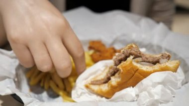 Fast food kafede patates kızartması, tavuk ve hamburger yiyen kadın, yemek yakın çekim.