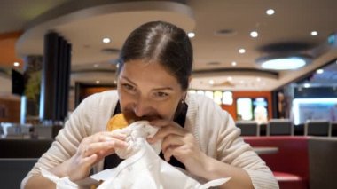 Genç esmer kadın gıda mahkemede fast food restoranda burger yiyor.