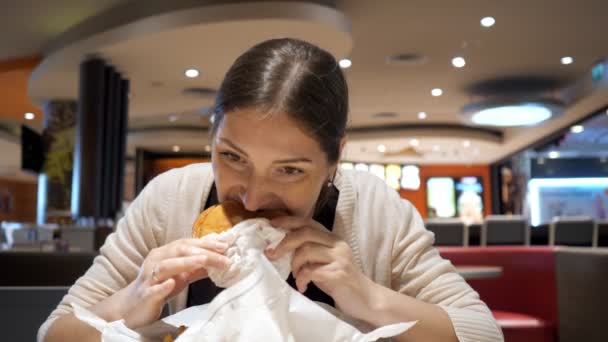 Mujer morena joven está comiendo hamburguesa en restaurante de comida rápida en patio de comidas . — Vídeo de stock