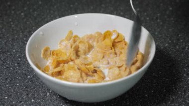 Adam kaşıkla kasede mısır gevreği ve süt karıştırma ve kahvaltı için yiyor.